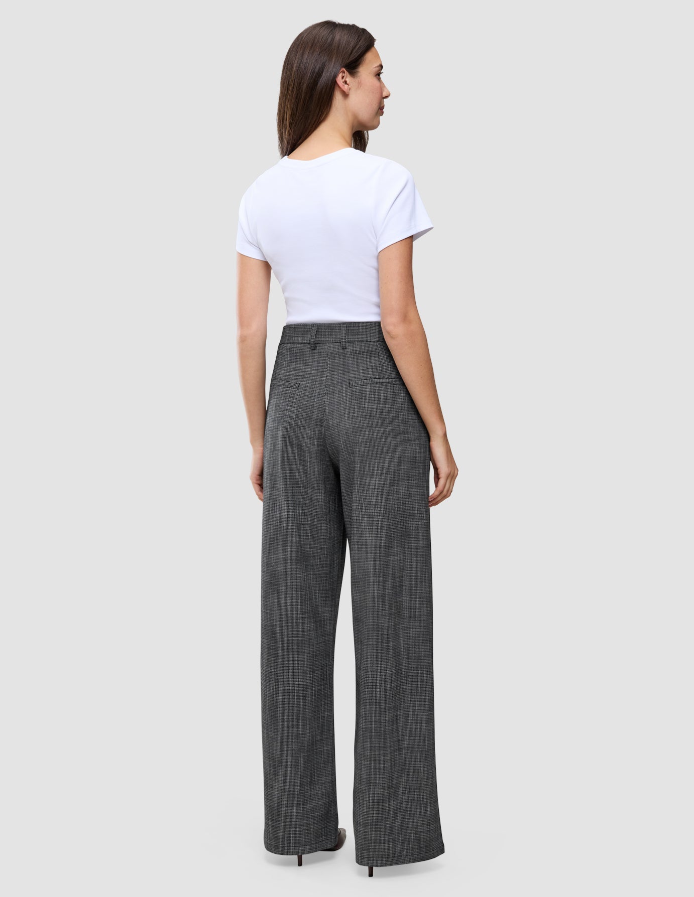 Eine Frau, von hinten gesehen, die ein weißes T-Shirt und eine graue Women Nara Pants Wide Black Check mit dezentem Gittermuster und hoher Taille trägt.